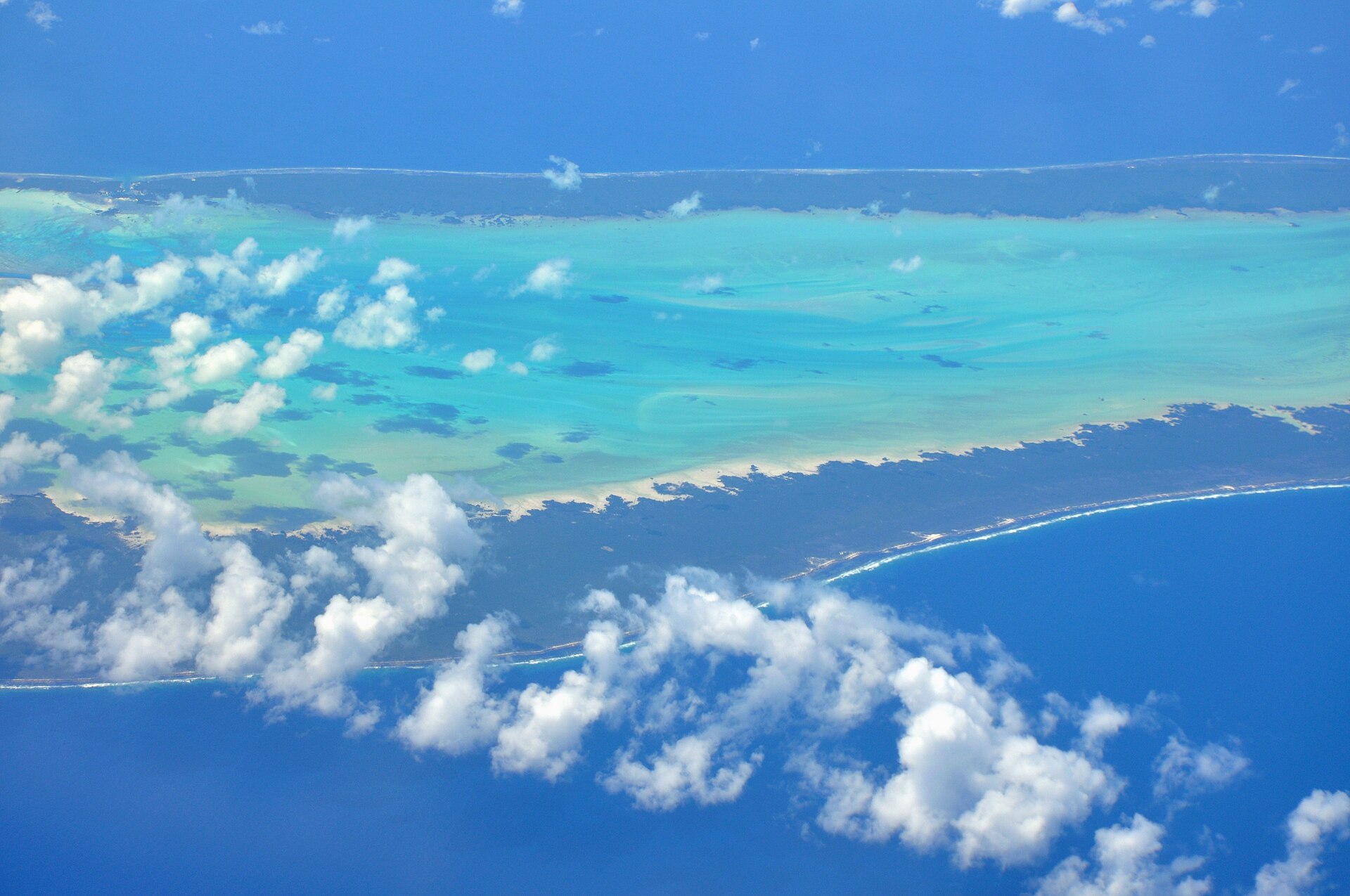 An outer island and its reef seen from an aircraft, cloud below