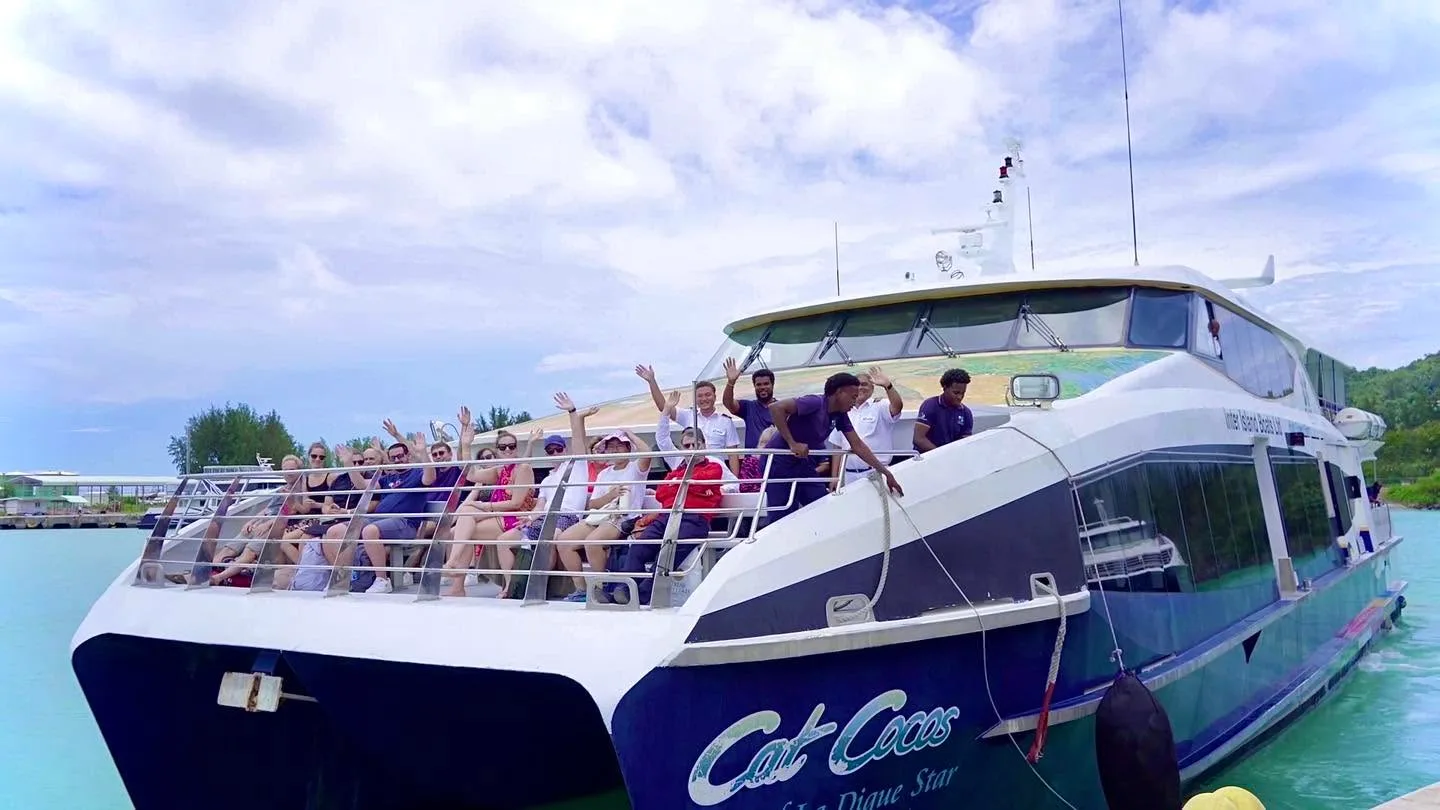 Passengers on the open top deck of a Cat Cocos catamaran, arms up, at the jetty