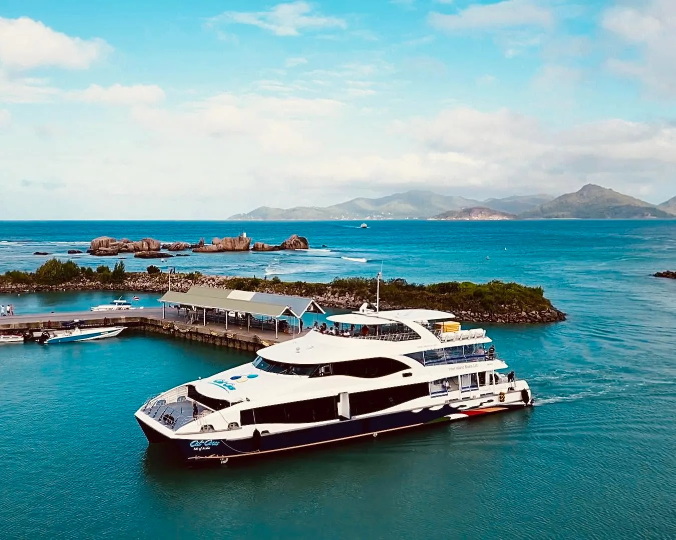 A Cat Cocos catamaran alongside the jetty, granite islet and green hills behind