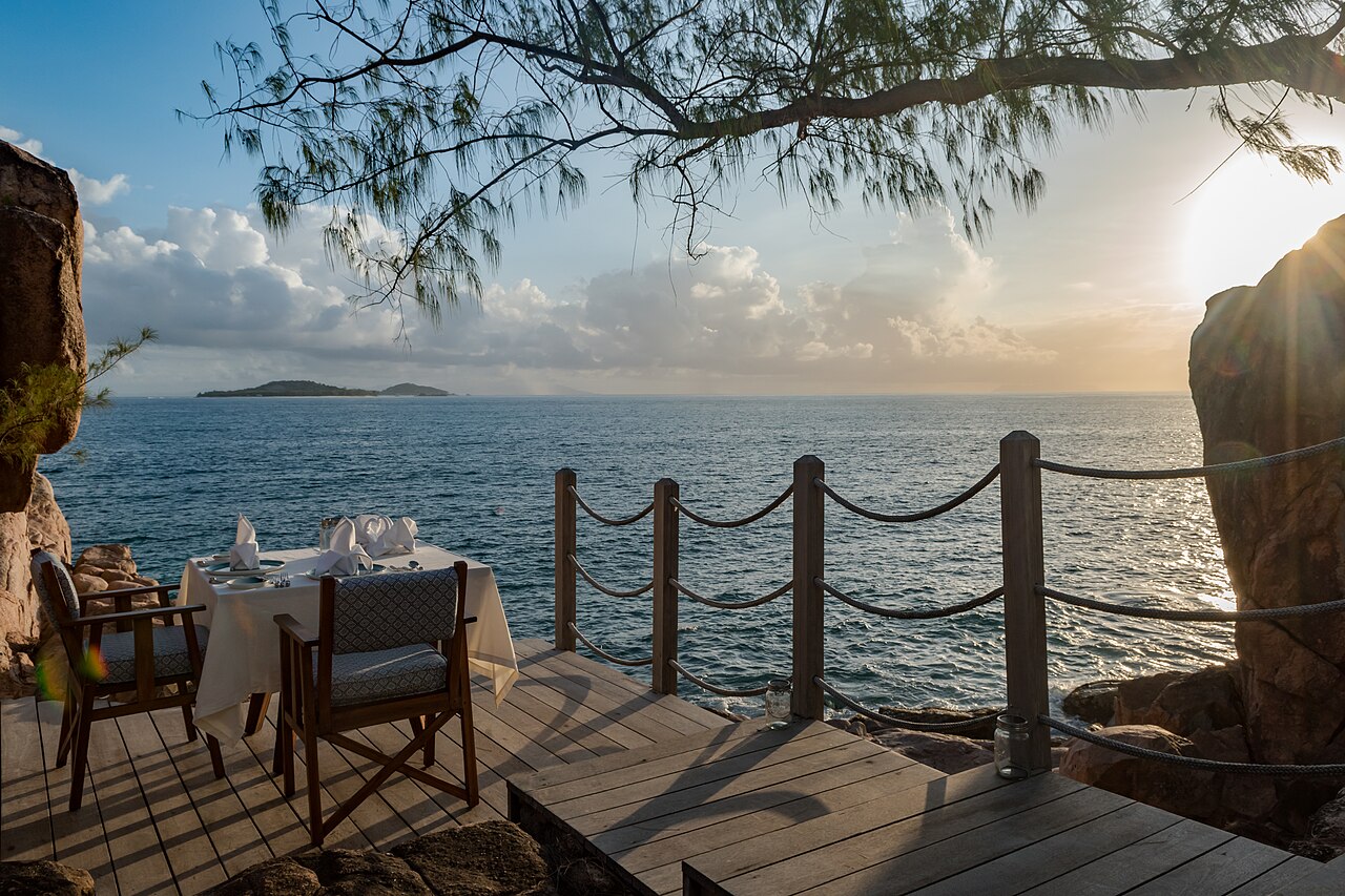 A restaurant terrace laid for dinner above the water on Praslin, at sunset.
