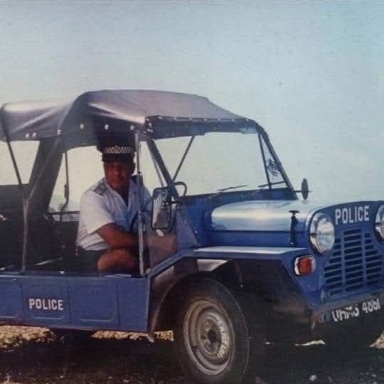 An archive photograph of a police officer at the wheel of a dark blue Mini Moke marked POLICE