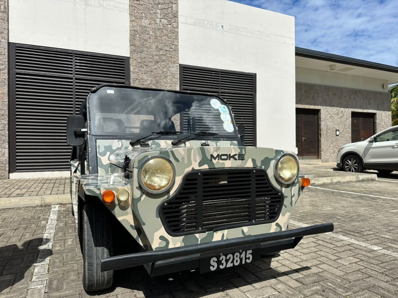 A Mini Moke in camouflage paint parked on a Mahé street