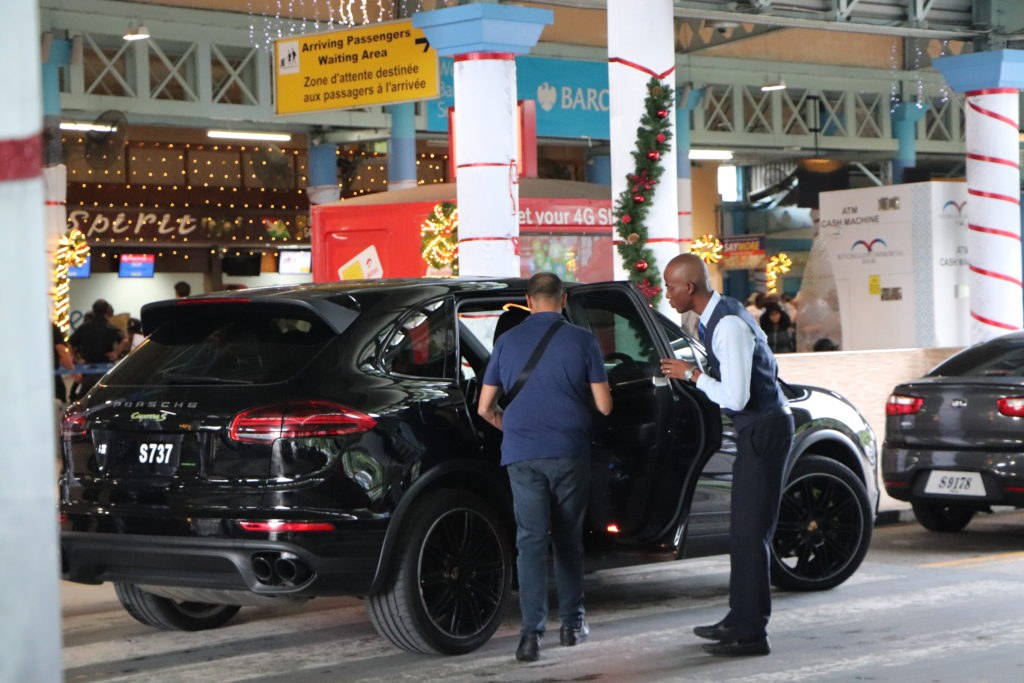A dark premium car at the arrivals kerb at Seychelles International with a driver holding the door