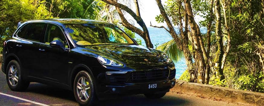 A dark premium car on a shaded coastal road under overhanging trees