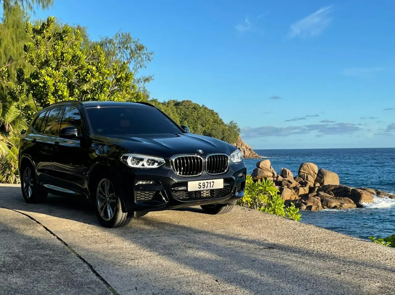 A dark premium car parked on a coast road above granite boulders and open sea