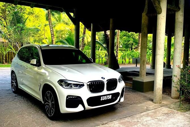 A pale premium car waiting under a timber pavilion with jungle behind