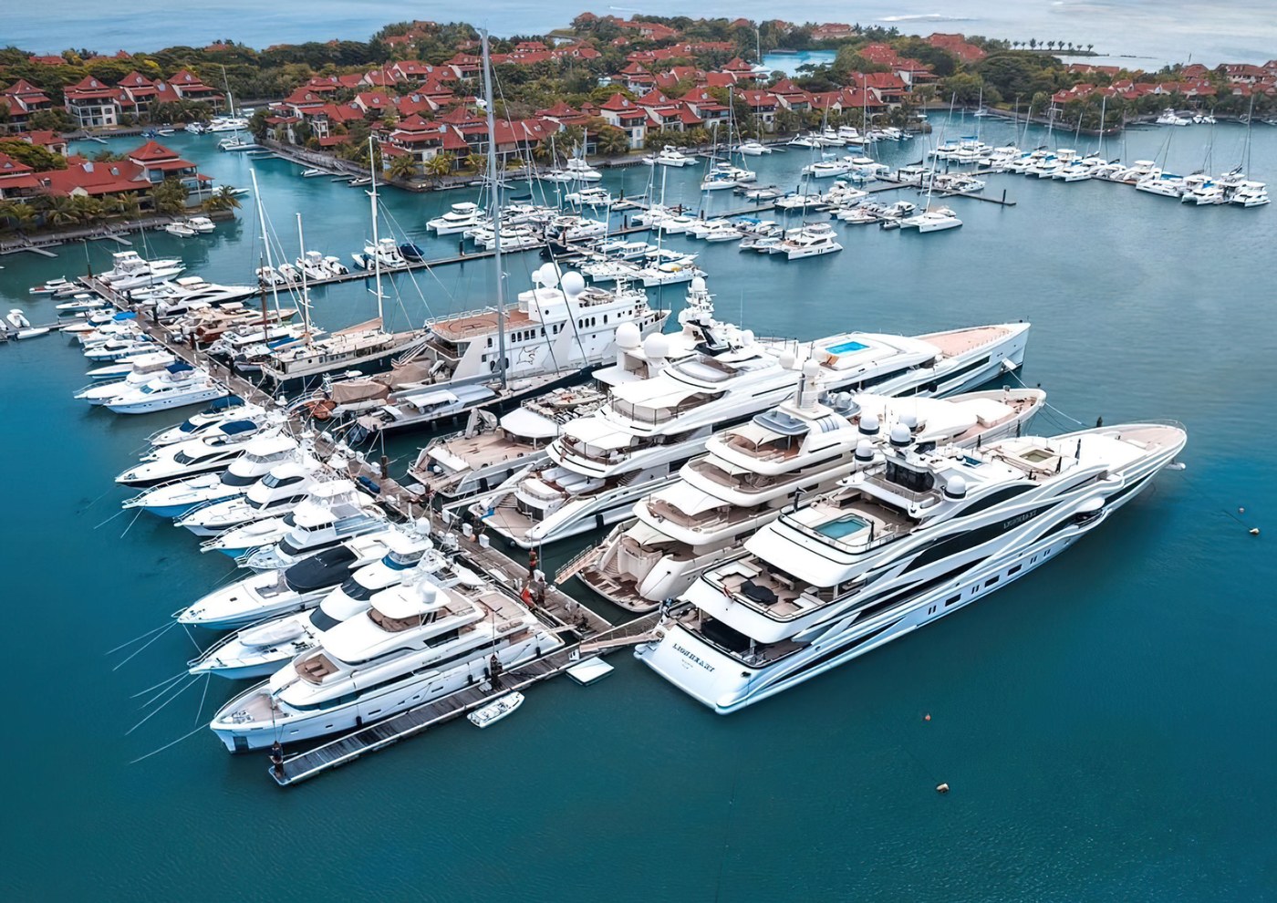 Superyachts moored in rows at the Eden Island marina, seen from the air, with the red-roofed development behind