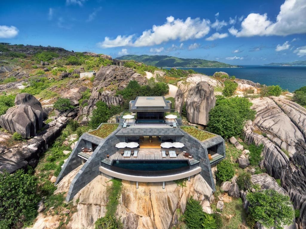 A residence seen from directly above, its terraces set down between granite boulders on a wooded headland