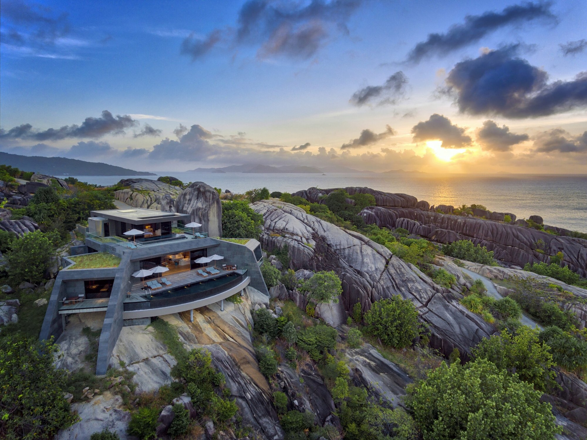 A modern residence built low into a granite headland above the sea at sunset, Seychelles