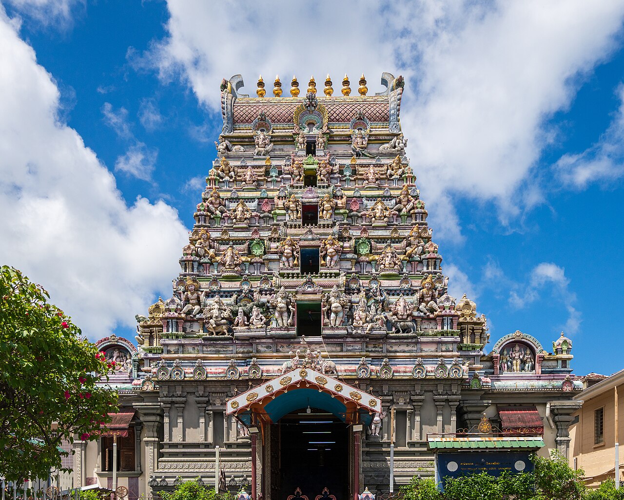 The gopuram of the Arul Mihu Navasakthi Vinayagar temple in Victoria seen head on, its tiers crowded with painted figures under a blue sky.