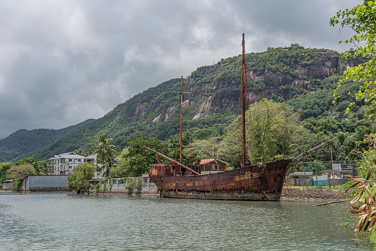 An abandoned wooden sailing boat in the shallows at Victoria, Mahé, with the granite ridge of Morne Seychellois behind