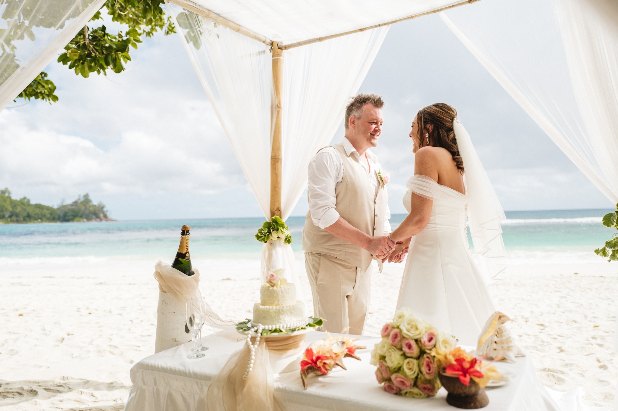 The couple hand in hand beside the dressed cake table on the sand