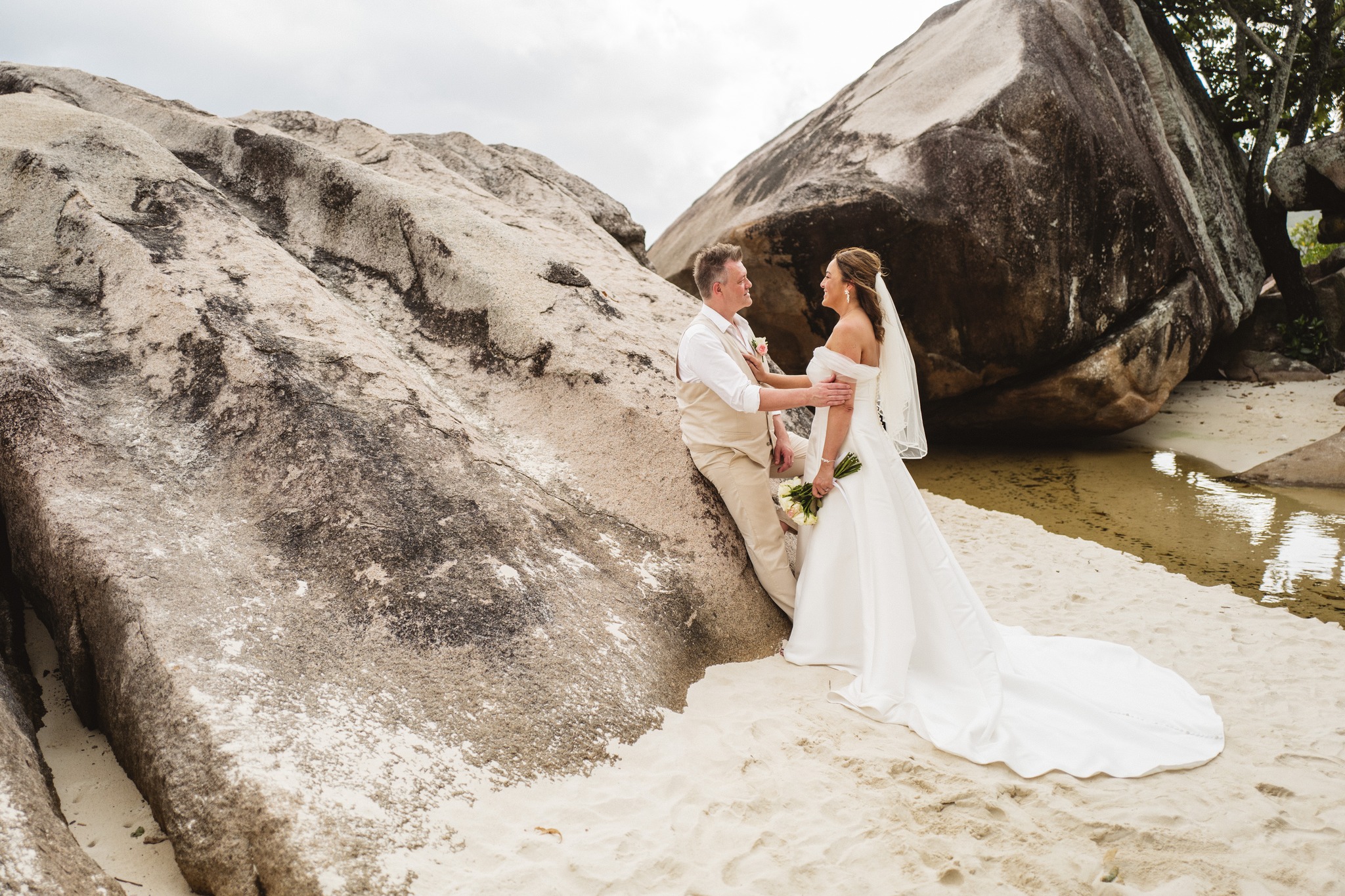 The couple standing close between two enormous granite boulders on the sand