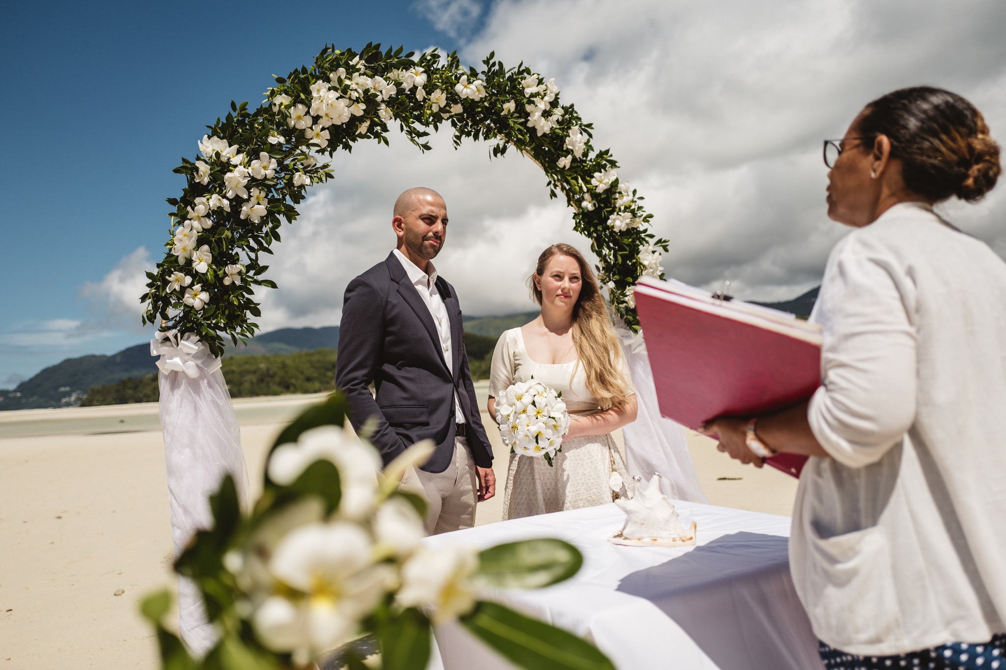 The celebrant reading at a flower arch while the couple listen