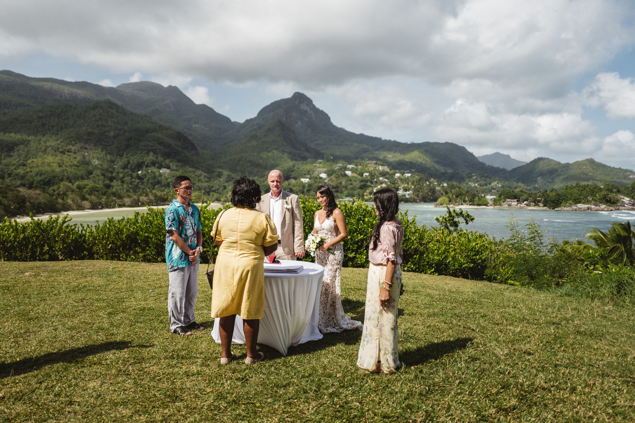 The small ceremony party standing on the lawn, the sea and the hills below them