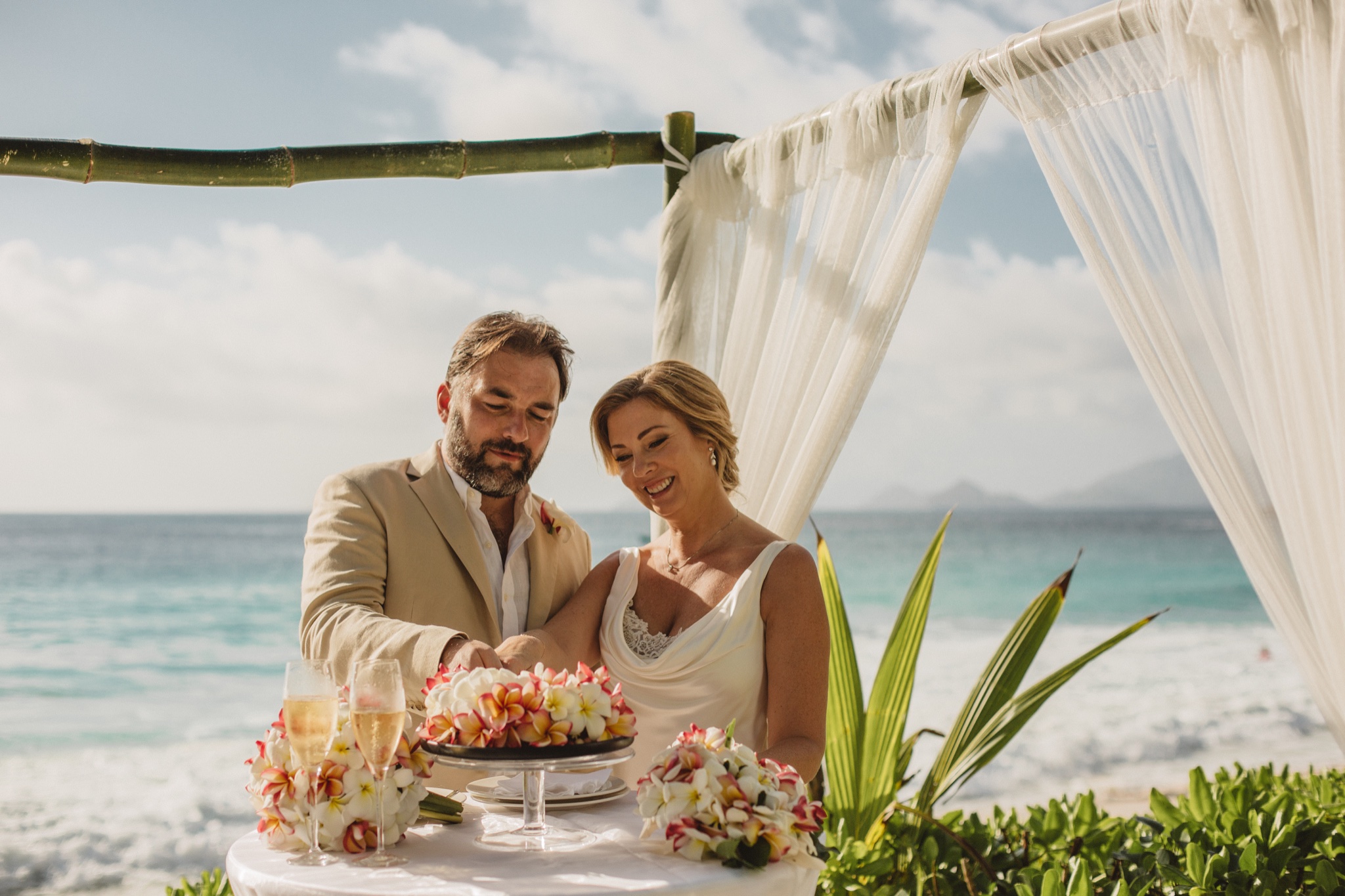 The couple seated at the ceremony table under white drapes, flowers between them