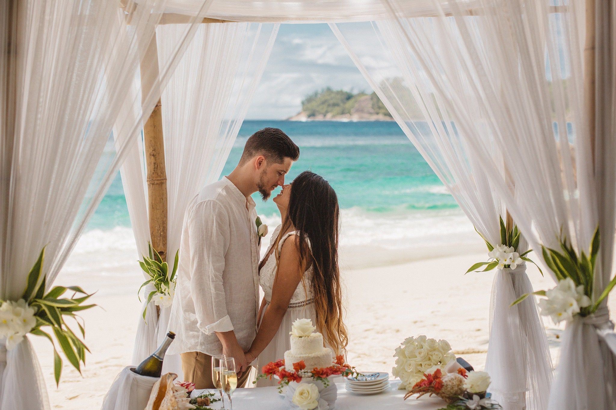 The couple kissing under a draped frame, the cake table in front, an islet framed between them