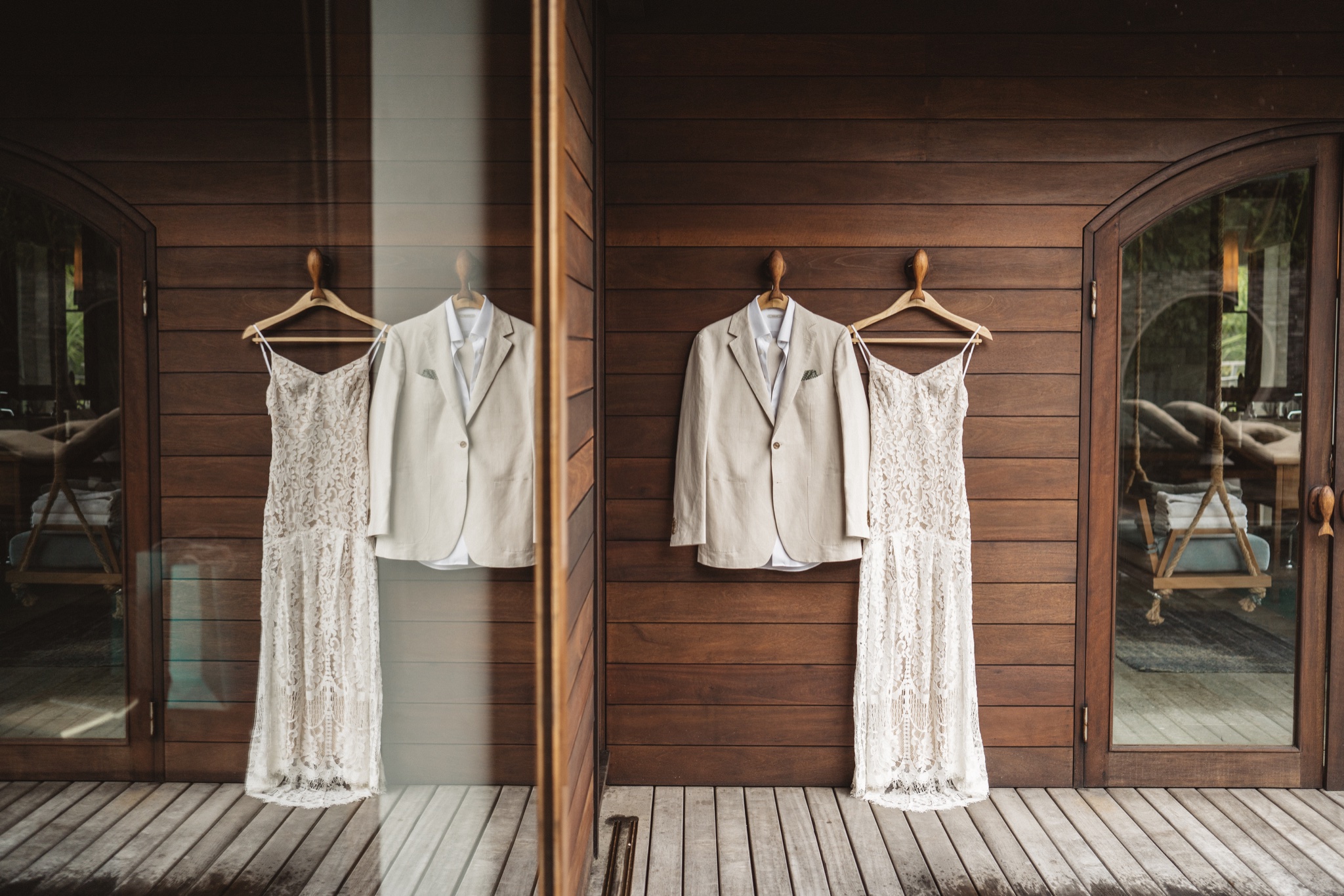 Two lace dresses and two linen jackets hanging along a timber verandah before the ceremony