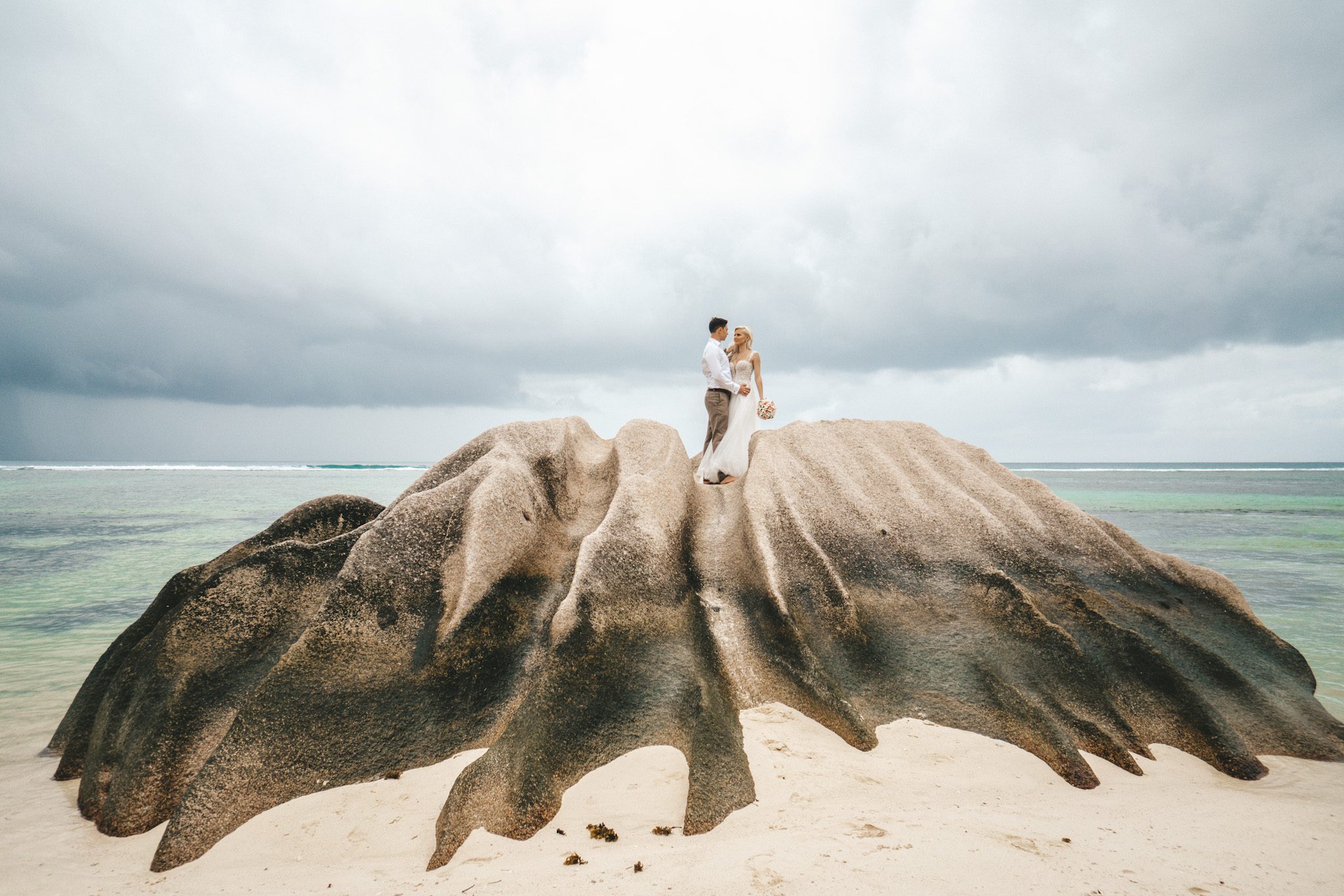 The couple standing on a fanned granite outcrop on an empty beach under a big sky
