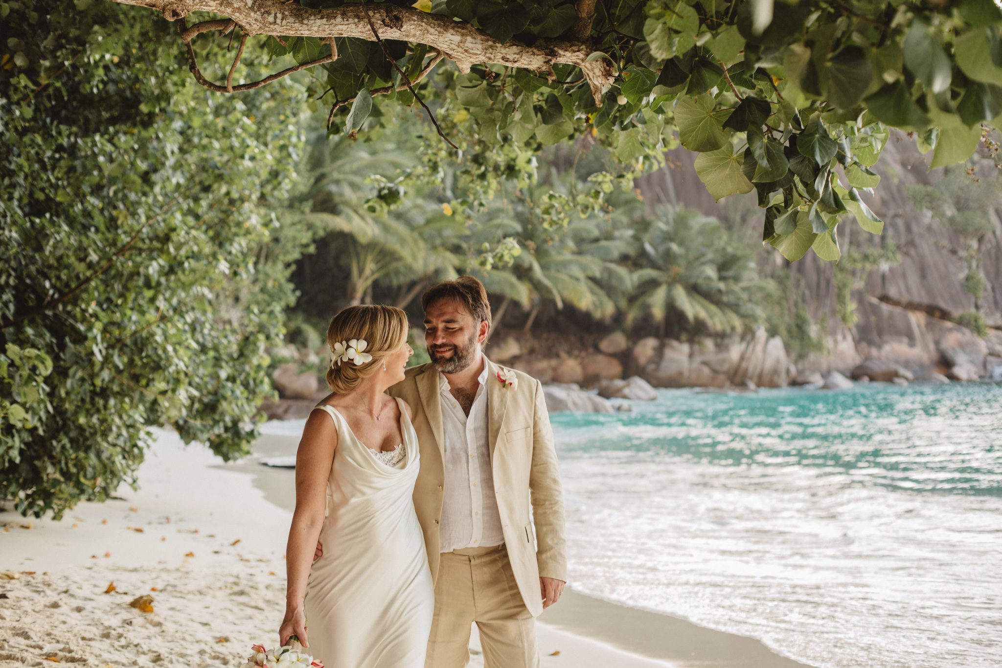 The couple walking the shore under an overhanging branch, a frangipani in her hair