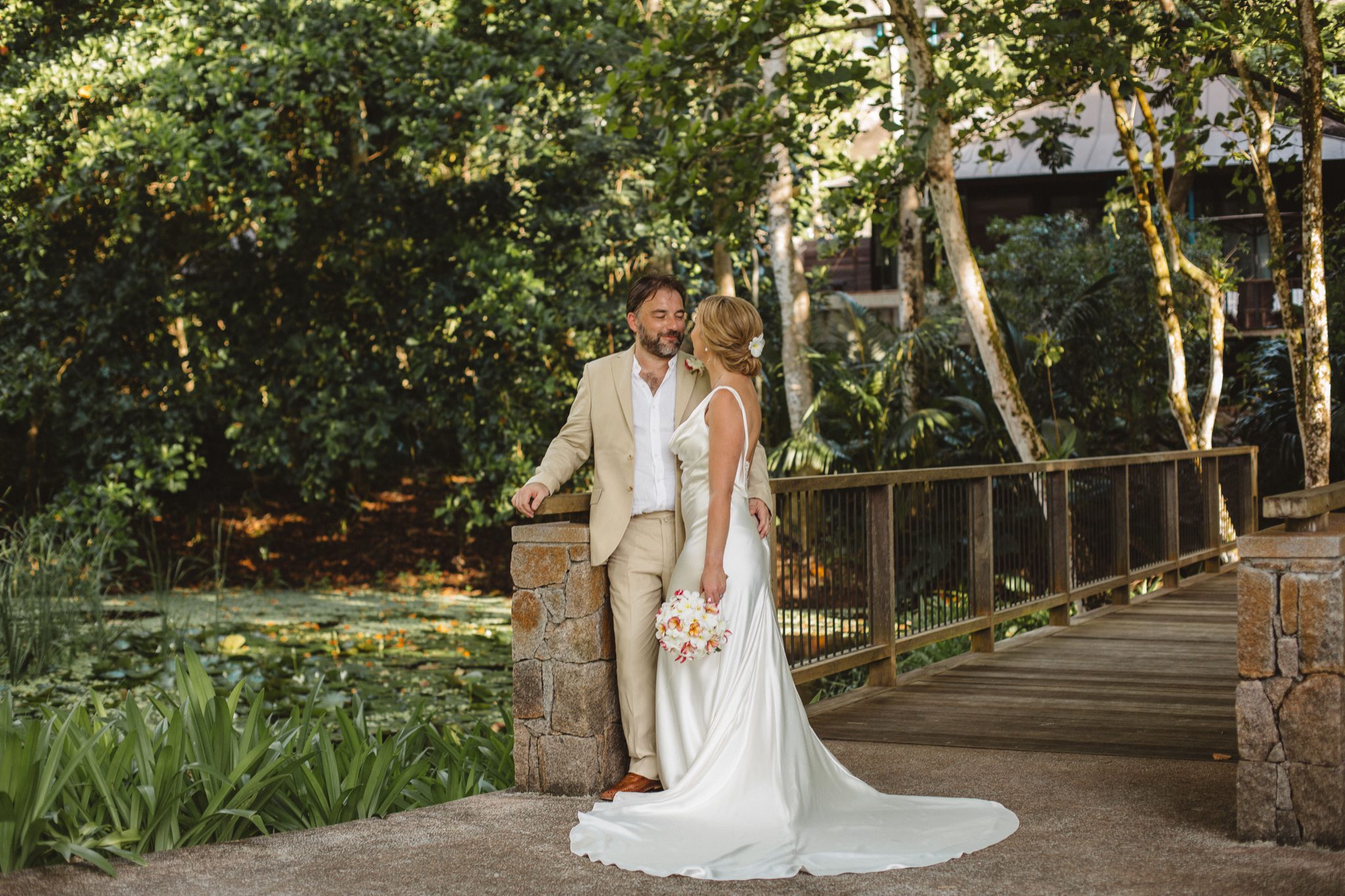 The couple hand in hand on a garden bridge, the lodge behind them