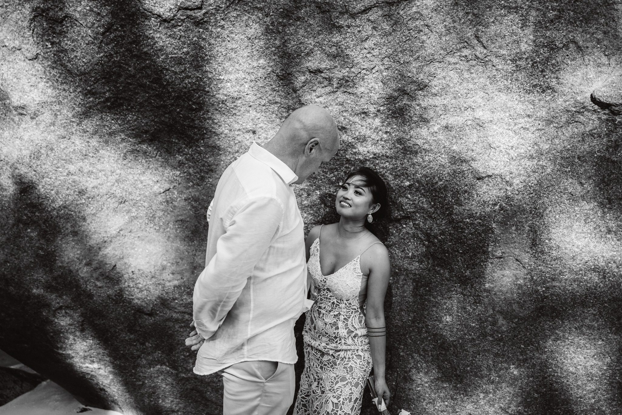 Black and white: the groom leaning in to his bride against a shadowed granite wall