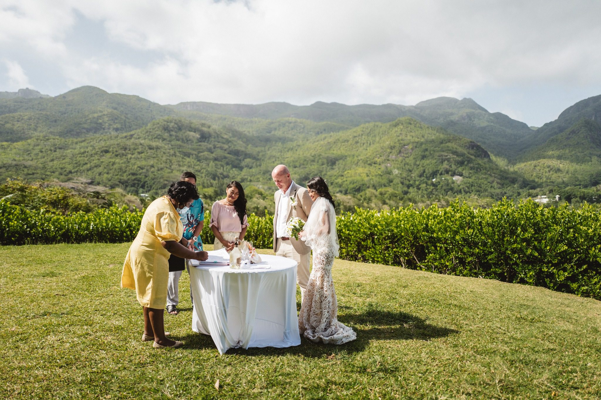 An outdoor ceremony on a hilltop lawn, the celebrant and witnesses at a dressed table