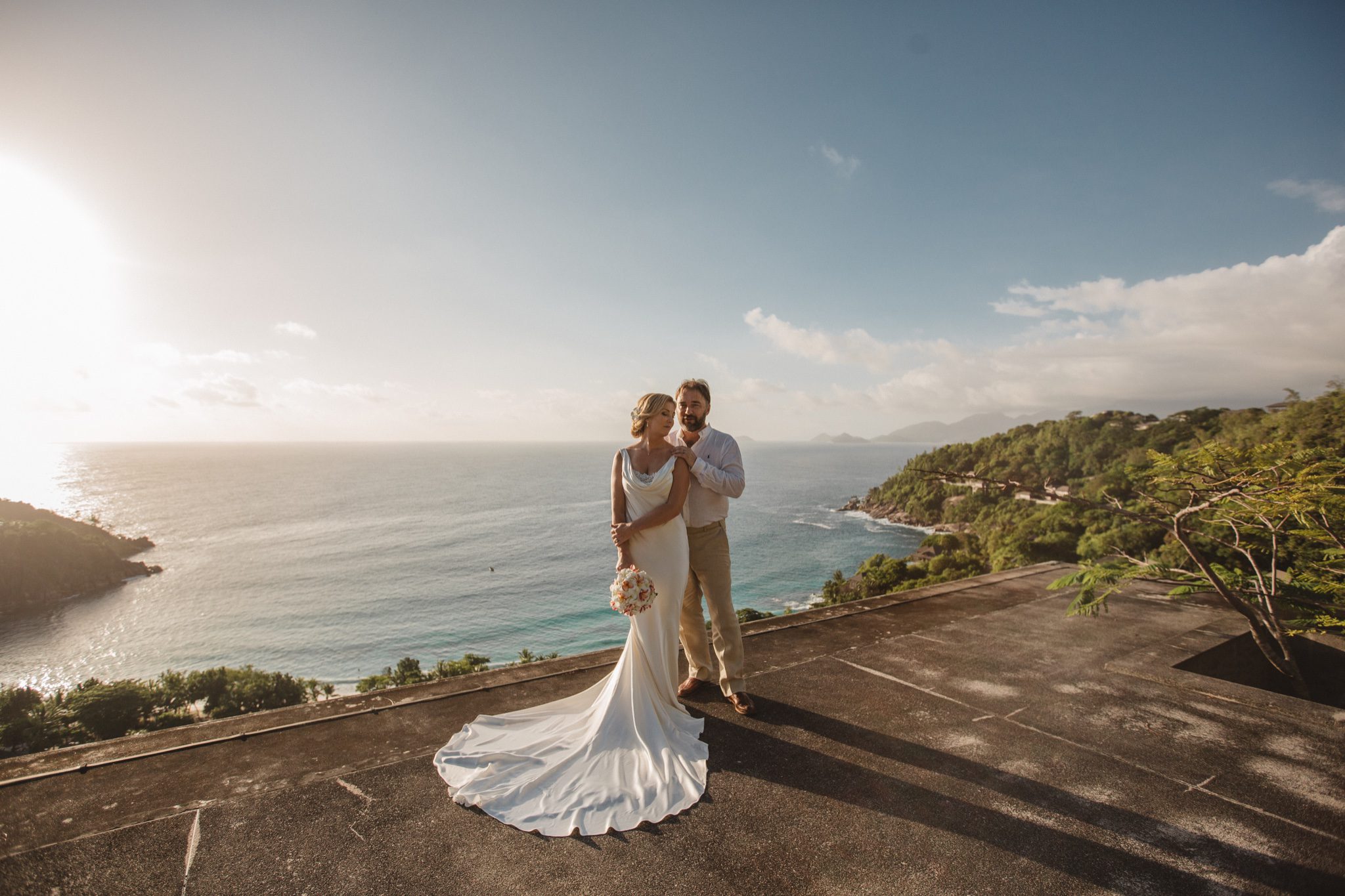 The bride's train spread across a hilltop terrace at sunset, the coast far below
