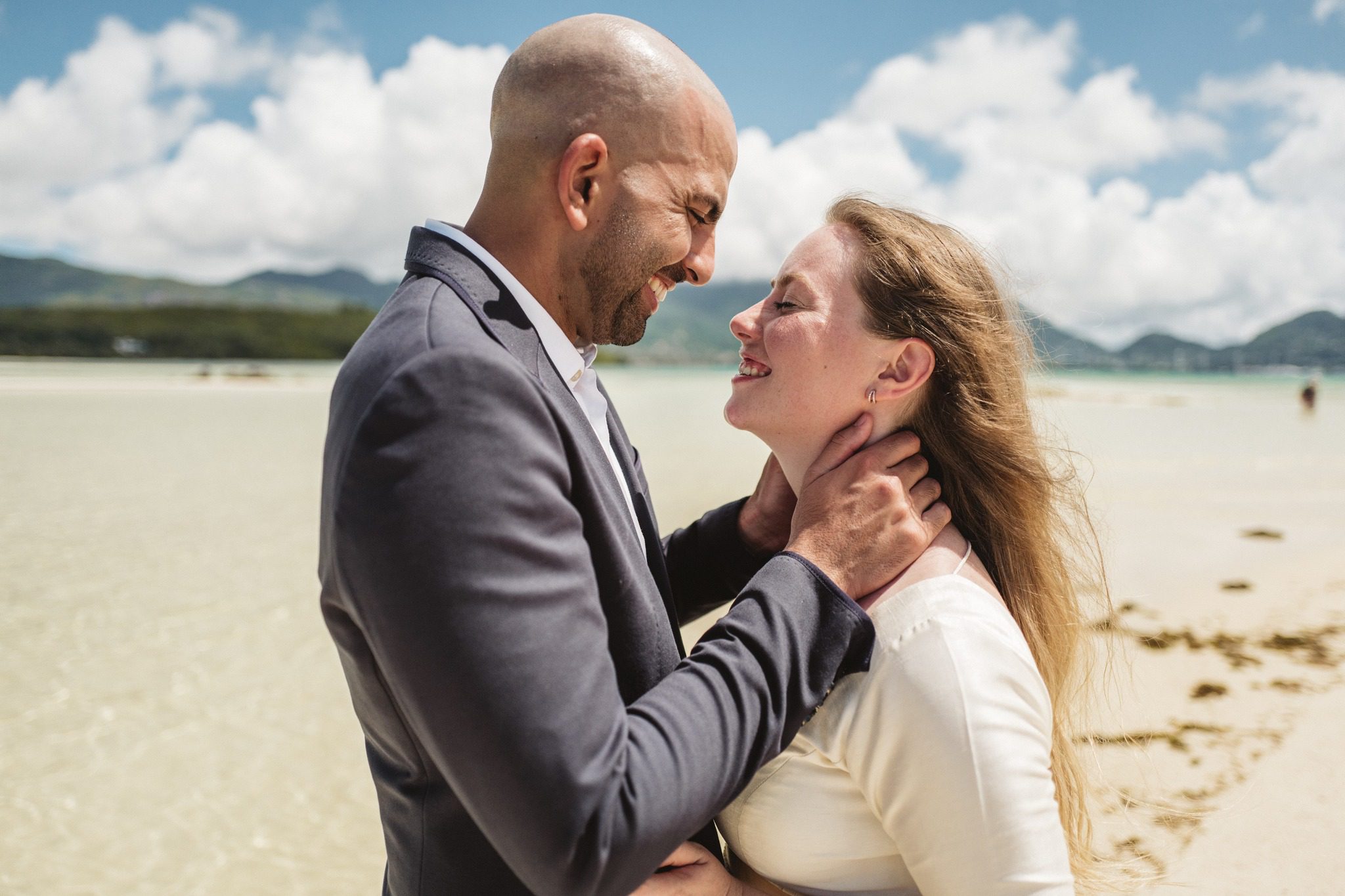 The groom holding the bride's face, both of them laughing, the shallows behind