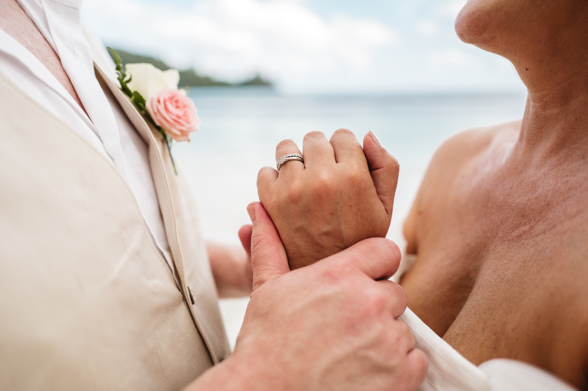Close on their joined hands, the groom's rose buttonhole in the foreground