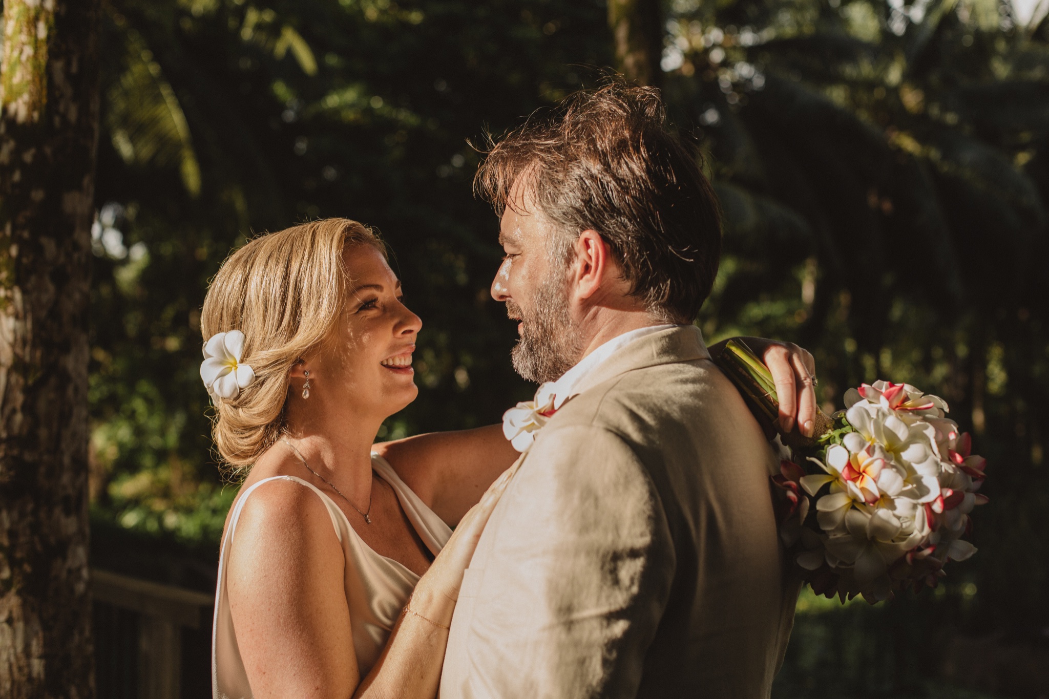 The couple laughing at the ceremony, frangipani in her hair