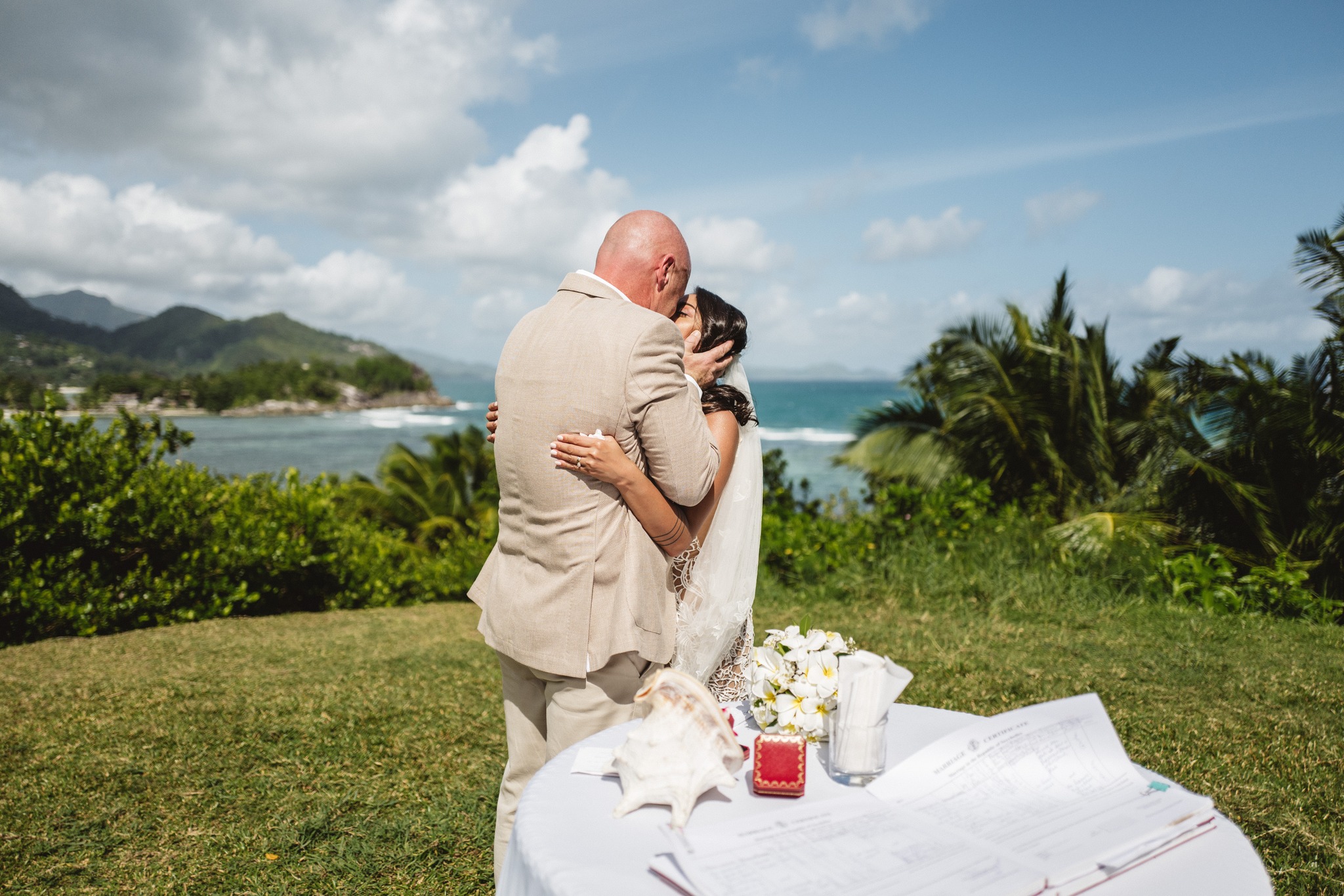 The couple holding each other on a lawn above the bay, the signing table beside them