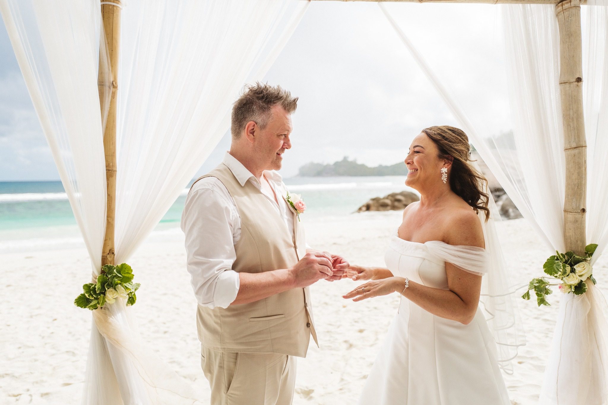 The groom putting the ring on under the canopy, both of them laughing