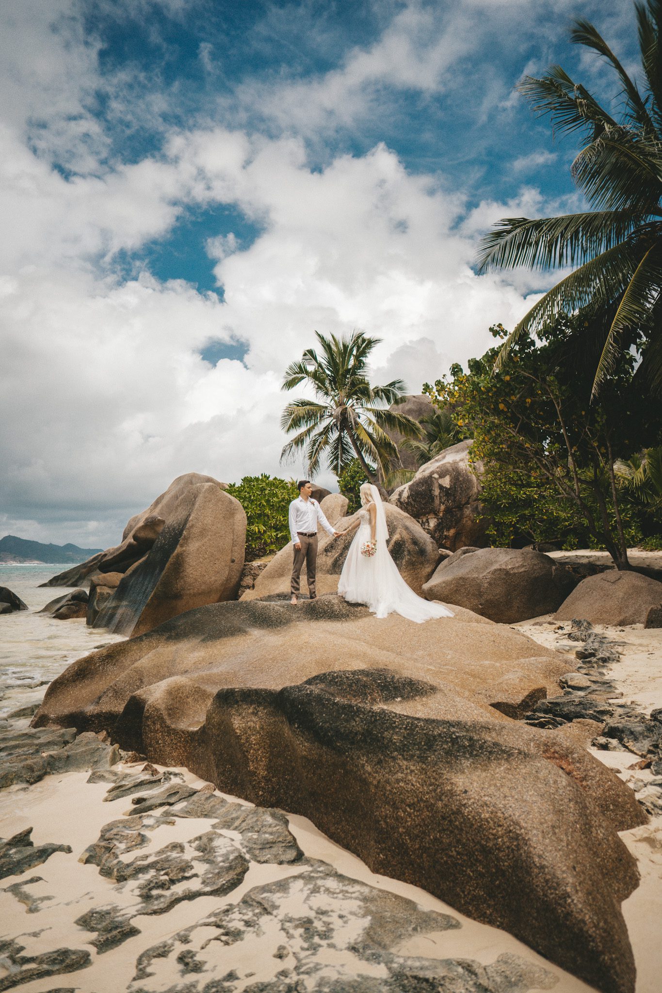 The couple on a rock under palms, cloud stacked behind them