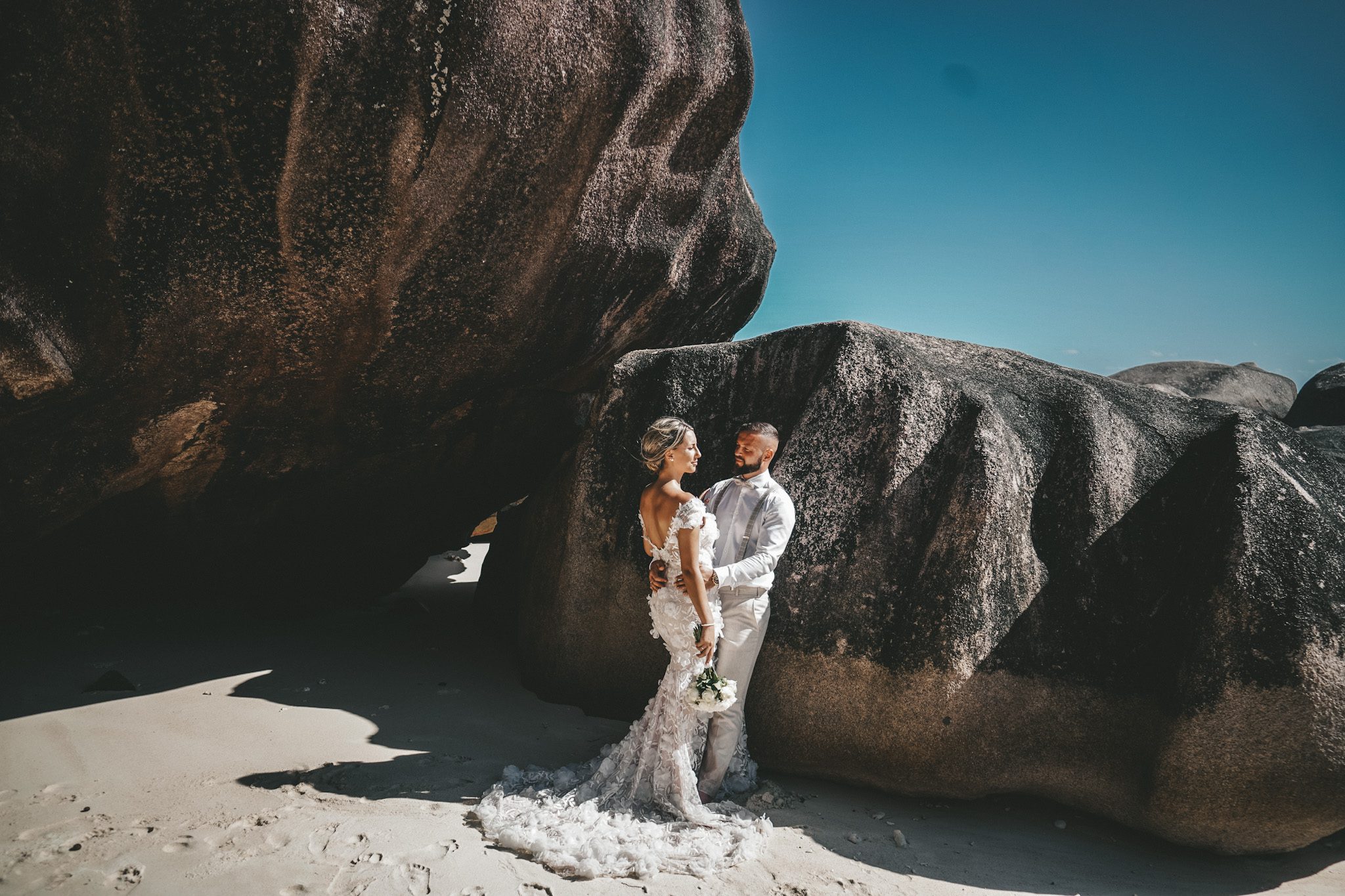 The couple in the shade of a great granite boulder on white sand