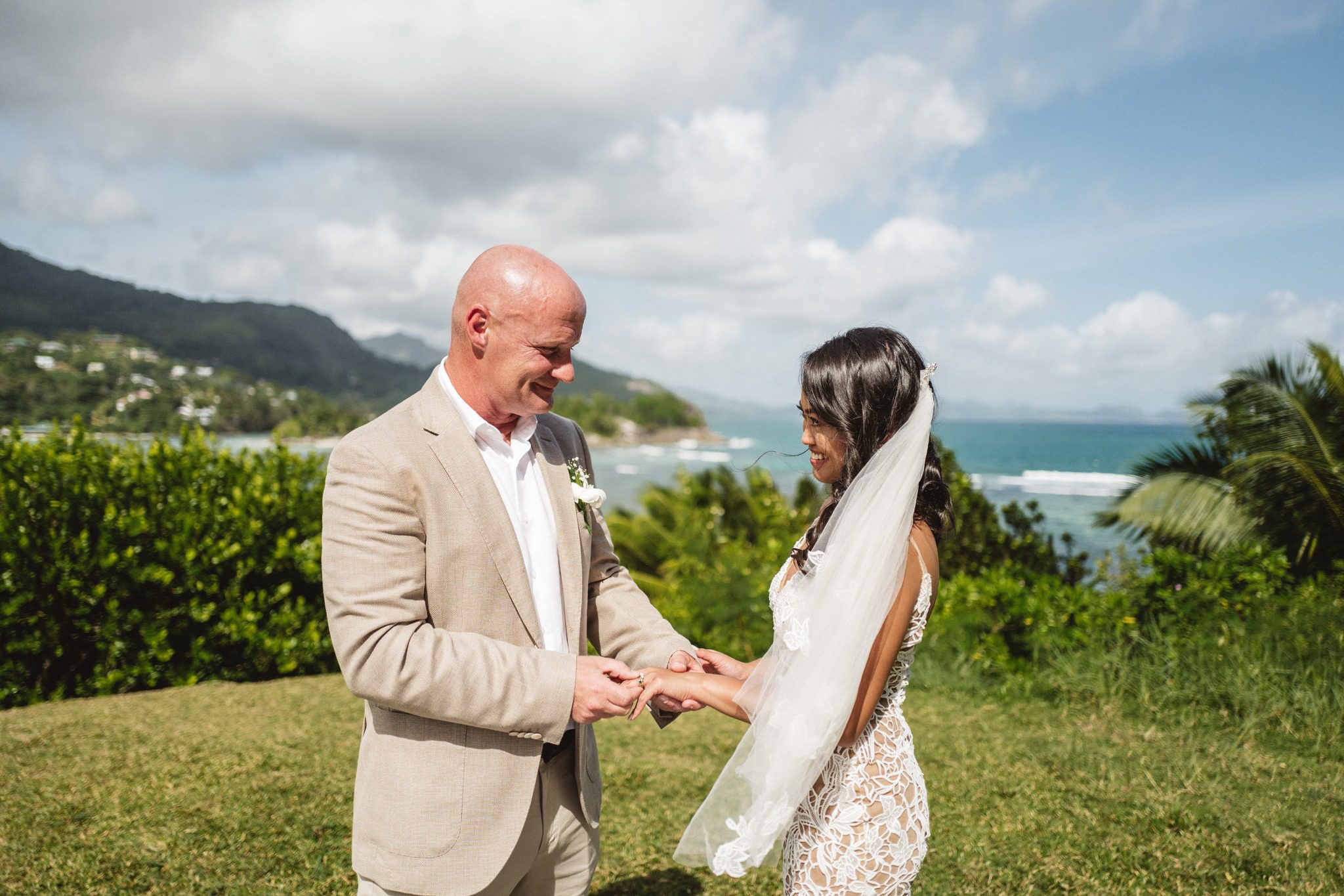 The groom taking the bride's hand at the ceremony, her veil lifting, the coast behind