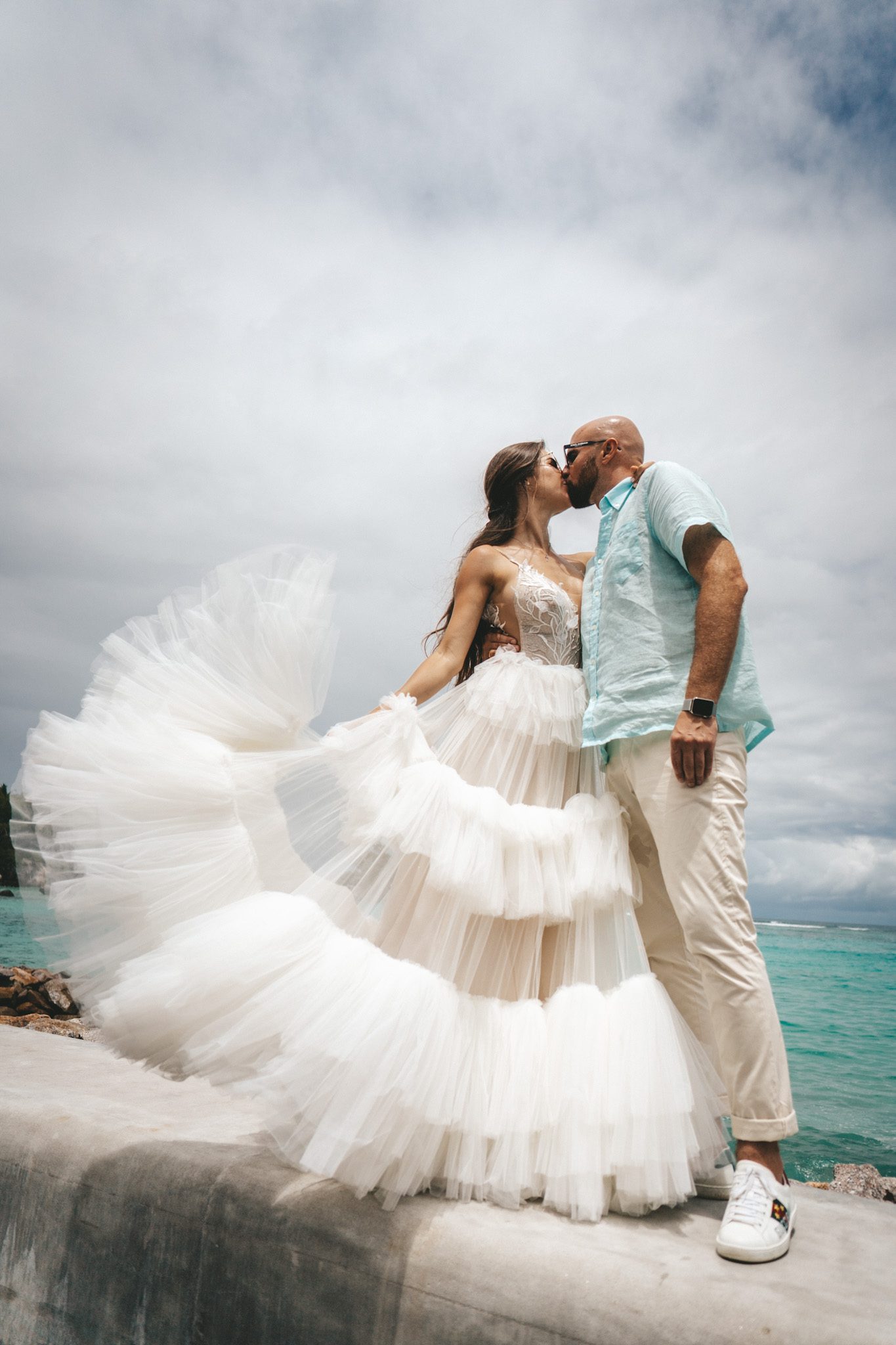 The bride's tiered skirt swinging as they kiss on the rocks