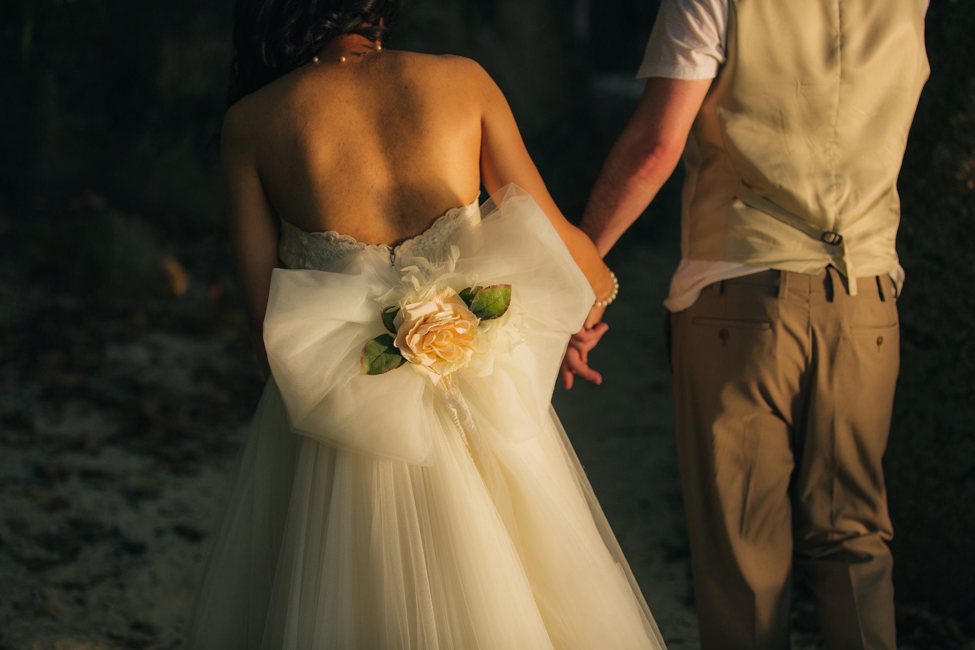 From behind: her tulle skirt and their joined hands in warm evening light