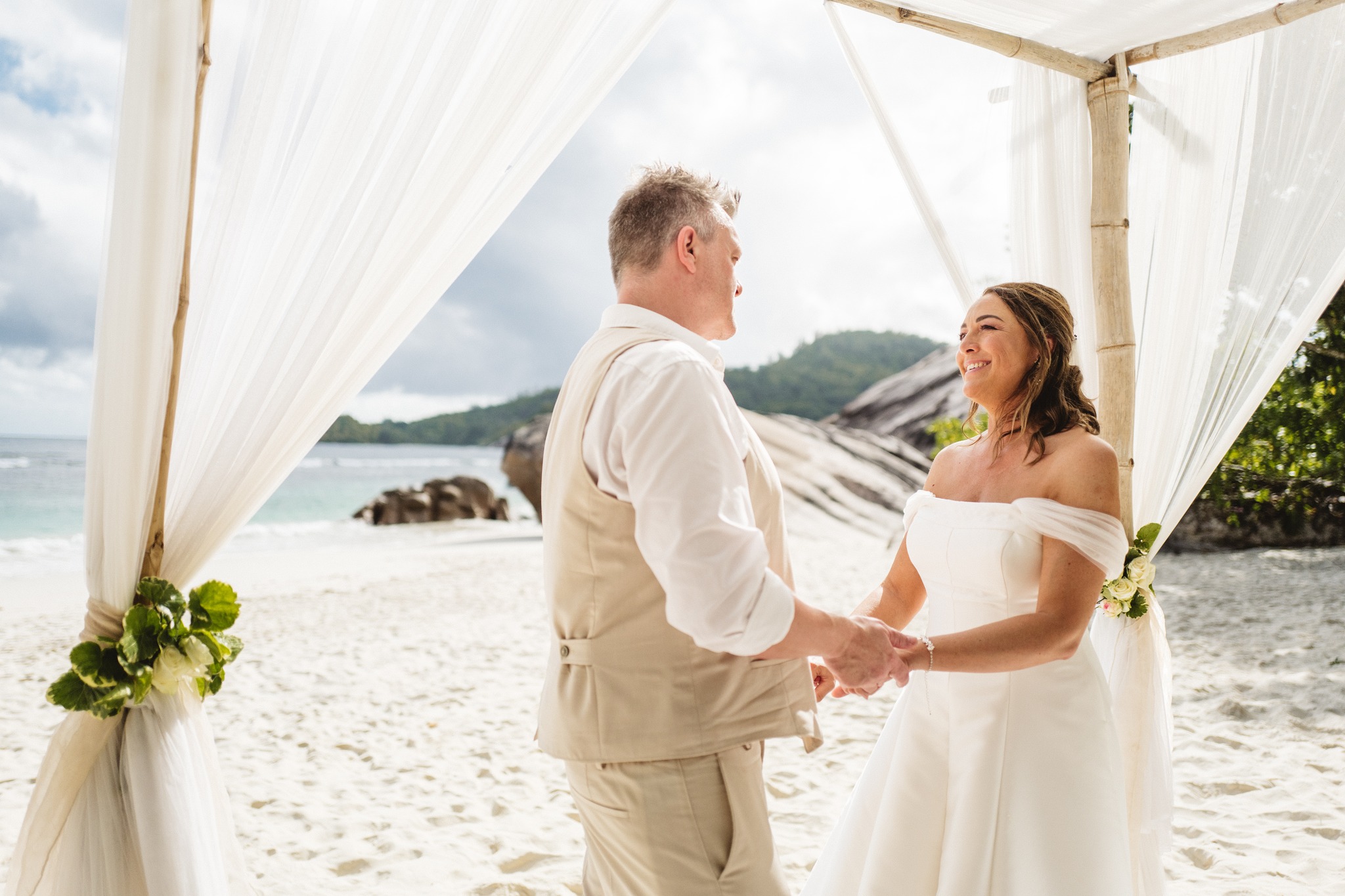 The couple holding both hands under a bamboo canopy hung with white drapes