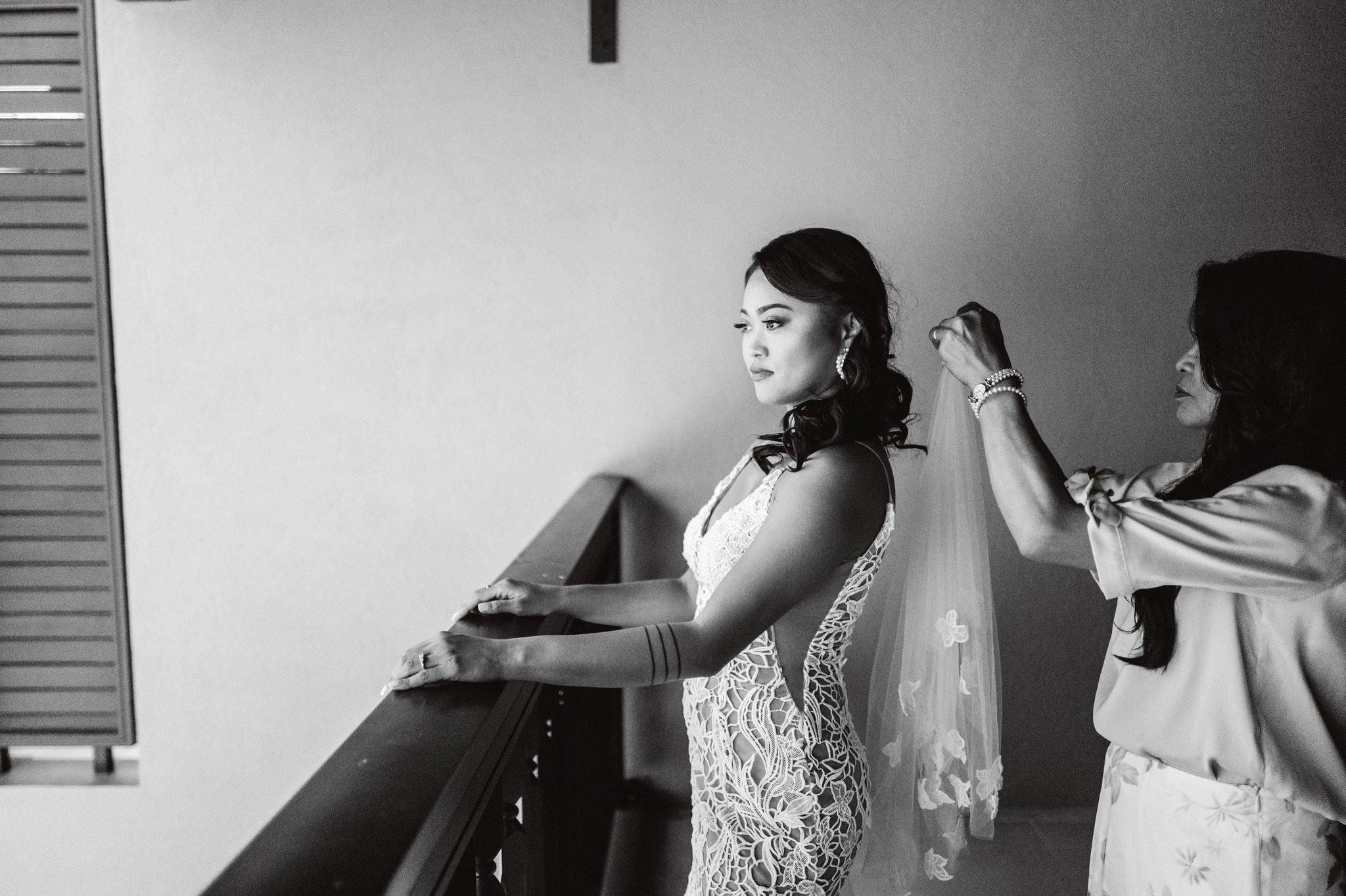 Black and white: a dresser fastening the bride's veil at a window