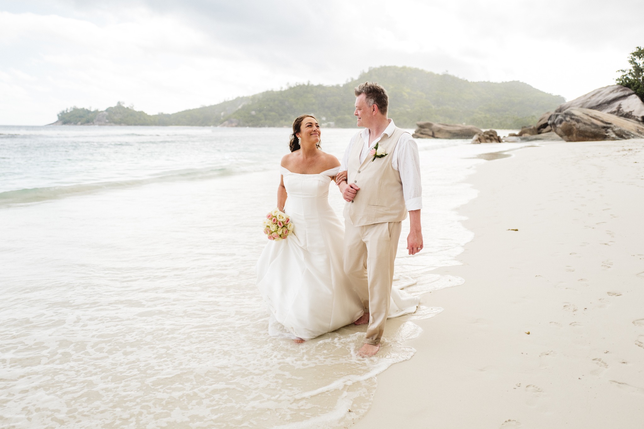 The couple walking the shoreline hand in hand, an islet across the water